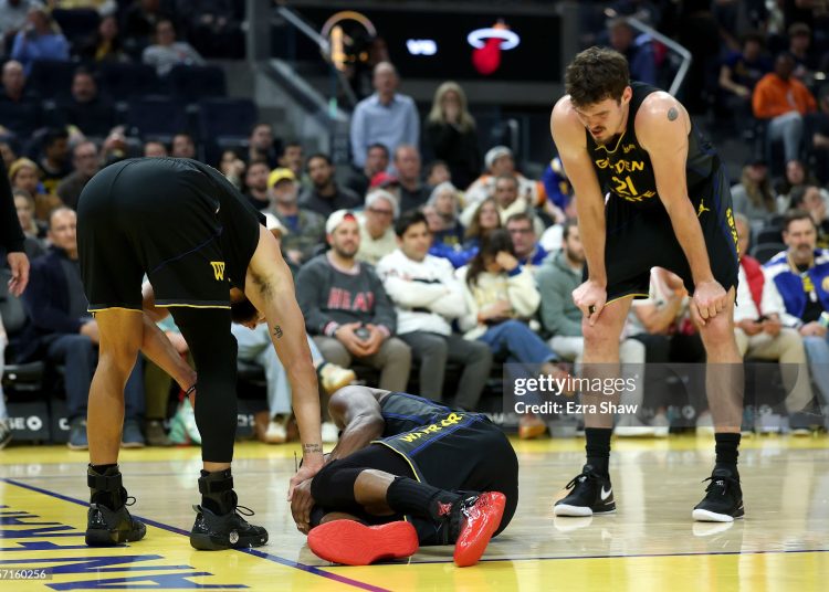 Jimmy Butler III #10 of the Golden State Warriors is looked at by Stephen Curry #30 and Quinten Post #21 after he collided with Davion Mitchell #45 of the Miami Heat and injured his knee during the third quarter (Photo by Ezra Shaw/Getty Images)