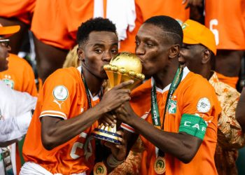 Ivory Coast's forward #15 Max-Alain Gradel (R) and Ivory Coast's forward #24 Simon Adingra (L)kiss the Africa Cup of Nations trophy on the podium after Ivory Coast won the Africa Cup of Nations (CAN) 2024 final football match between Ivory Coast and Nigeria at Alassane Ouattara Olympic Stadium in Ebimpe, Abidjan on February 11, 2024. (Photo by FRANCK FIFE / AFP) (Photo by FRANCK FIFE/AFP via Getty Images)